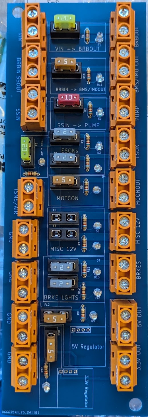 Populated fusebox PCB: rows of orange screw terminals top and bottom, blade fuses of varying ratings across the middle, an indicator LED under each fuse, and silkscreen labels for BRKE LIGHTS, MISC 12V, MOTCON, ESOK, PUMP, BMS/IMD OUT and the 3.3 V and 5 V regulator sections